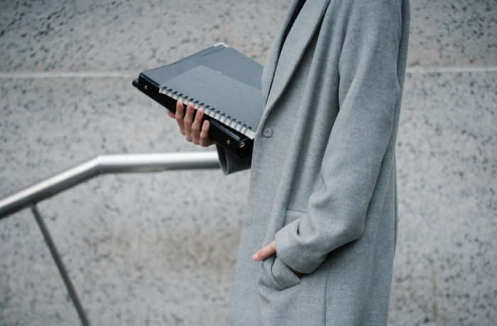 persoon in grijze lange jas met folders in hand