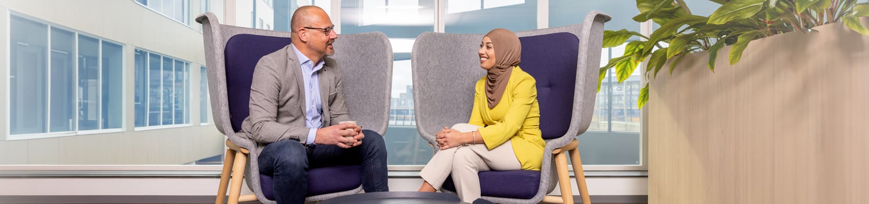 twee medewerkers hebben een gesprek op kantoor, zittend op grijze stoelen