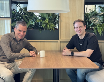 Twee collega's drinken koffie en kijken beide in de camera