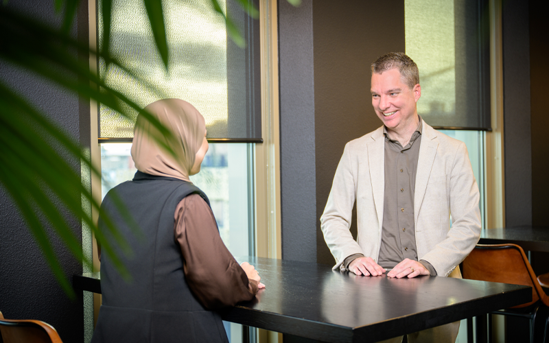 Banner 800×500 mobiel twee collega’s zijn met elkaar in gesprek aan tafel