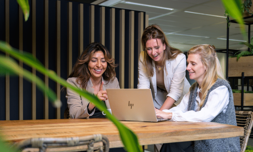 Drie collega's lachen en zijn achter één laptop aan het werk