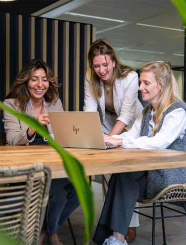 Drie collega's lachen en zijn achter één laptop aan het werk
