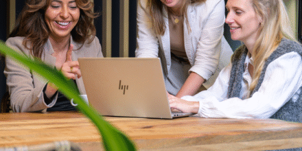Drie collega's lachen en zijn achter één laptop aan het werk