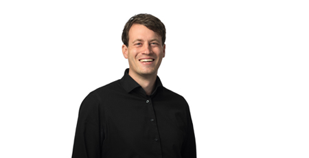 Color portrait photo of a smiling man wearing a black shirt.