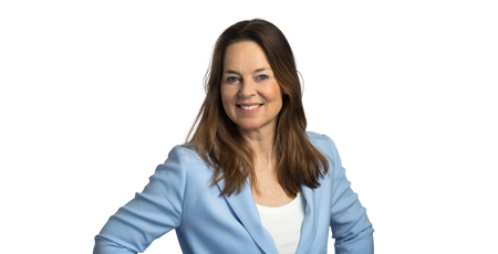 Color portrait photo of a smiling woman standing with her hands on her hips, wearing a light blue blazer.