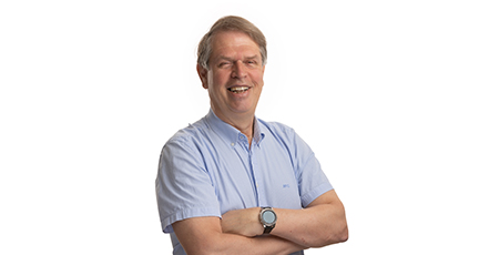 Color portrait photo of a smiling man with his arms crossed, wearing a blue short-sleeved shirt.