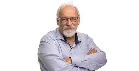 Color portrait photo of a bearded person wearing glasses and a light blue shirt, standing with arms crossed.